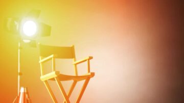 كرسي مخرج خشبي مع ضوء كشاف ساطع في خلفية ملونة، يرمز إلى صناعة السينما والإنتاج الفني.