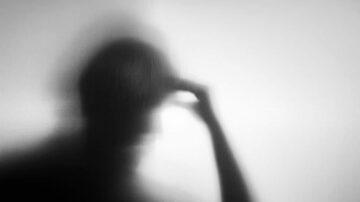 ظل شخص يمسك برأسه، يظهر بشكل ضبابي على خلفية فاتحة، يعكس شعوراً بالقلق أو التفكير العميق.