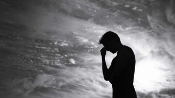 شخص واقف في الظل يمثل مشاعر الحزن أو التأمل، مع سماء مليئة بالسحب الداكنة في الخلفية.