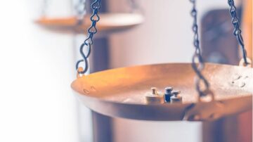 ميزان قديم مع وزنين صغيرين، يوضح توازن القوى. الخلفية ضبابية مع تركيز على الأداة، مما يبرز تفاصيل التصميم.