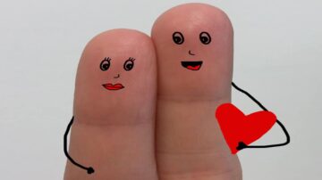 صورة تظهر إصبعين مرسوم عليهما تعبيرات وجه تعكس الحب، مع يدين مرسومتين تحملان قلبًا أحمر. تعبر الصورة عن مشاعر الرومانسية والود.