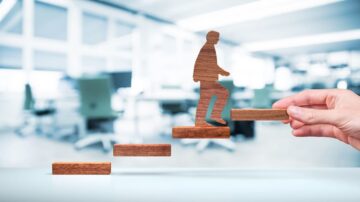 صورة توضح شخصًا خشبيًا يصعد على درجات خشبية، مع خلفية مكتبية حديثة. تعبر الصورة عن مفهوم التقدم والنجاح في بيئة العمل.