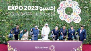 مجموعة تسقي النباتات بمرشات سوداء أمام حديقة عمودية و"إكسبو 2023، الدوحة، قطر".