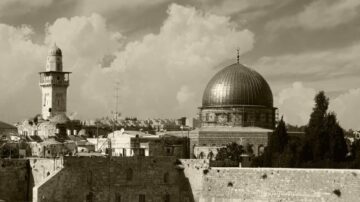 منظر لمدينة القدس يظهر قبة الصخرة ومئذنة المسجد الأقصى، مع سماء مليئة بالغيوم. الصورة بتدرجات اللونين الأبيض والأسود، تعكس التاريخ الغني والمعمار الإسلامي في المنطقة.