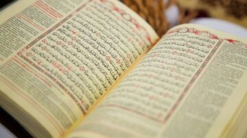 صفحة مفتوحة من مصحف القرآن الكريم، تظهر النصوص العربية مكتوبة بخط واضح، مع تمييز لبعض الآيات. الخلفية تحتوي على عناصر طبيعية تضيف لمسة دافئة.