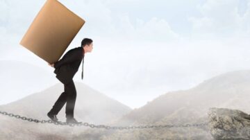 رجل يرتدي بدلة يحمل صندوقًا كبيرًا أثناء المشي على سلسلة فوق مناظر طبيعية جبلية ضبابية، مما يعكس تحديات وصعوبات في العمل أو الحياة.