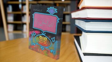 كتاب "ابن الحلال" مرئي على طاولة خشبية، محاط بمجموعة من الكتب. يغلب على غلاف الكتاب تصميم ملون مع رسومات فنية. الخلفية تحتوي على رفوف كتب.