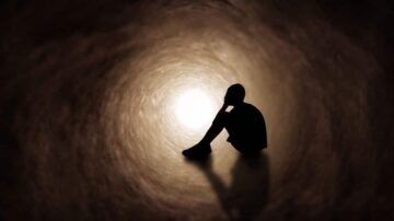 شخص يجلس في نهاية نفق مظلم، مع إضاءة خافتة تخرج من النهاية. يعبر عن الشعور بالوحدة والتأمل في الظلام.