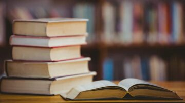 كتب مفتوحة ومكدسة في مكتبة، مع تركيز على كتاب مفتوح على الطاولة.