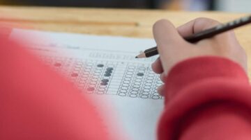 يد تظهر شخصًا يملأ استمارة اختبار أو استبيان بقلم رصاص على ورقة تحتوي على نقاط سوداء وبيضاء مرتبة في صفوف.