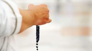 يد تحمل سبحة مصنوعة من حبات داكنة، بخلفية غير واضحة. تعكس الصورة أجواء من السكينة والتأمل الروحي.