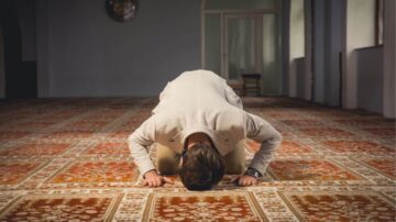 رجل يؤدي الصلاة على سجادة في مسجد، يضع جبهته على الأرض في وضع السجود، مع إضاءة طبيعية تحيط به.