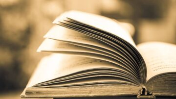 كتاب مفتوح بأوراق متقلبة، يظهر تفاصيل الصفحات بلون دافئ، مع خلفية ضبابية تضيف لمسة فنية.