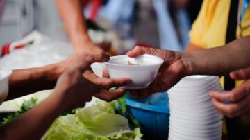 تبادل وعاء طعام في سوق، أيدٍ تقدم وتستقبل الوعاء، مع خلفية من الخضار الطازجة.