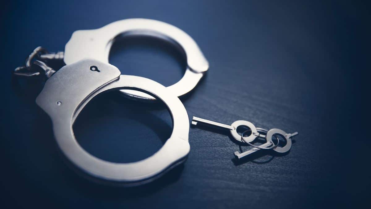 أصفاد فضية مفتوحة مع مفتاح صغير بجانبها على سطح داكن، تعبير عن الاعتقال أو الحرية.