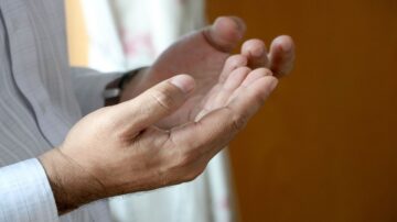 رجل يرفع يديه في وضع الدعاء، مع تركيز على تفاصيل اليدين. الخلفية غير واضحة، مما يبرز اليدين. تعبير عن الإيمان والروحانية.