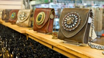 حقائب متدلية مزينة بتفاصيل فريدة وأزرار لامعة، مرتبة على رف خشبي في متجر. تعرض الحقائب تصاميم متنوعة وألوان دافئة، مع سلاسل معدنية تضيف لمسة أنيقة.