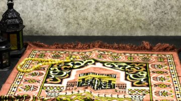 سجادة مزخرفة بتصميم تقليدي، تحتوي على نقوش ملونة، مع فوانيس إسلامية وسبحة بجوارها، تعكس الأجواء الروحانية.