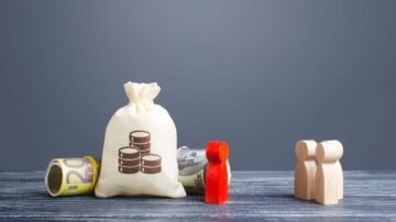 كيس من المال مع عملات ورقية يورو ودولار، بالإضافة إلى شخصيتين خشبيتين. يرمز إلى المفاهيم المالية والاستثمار.