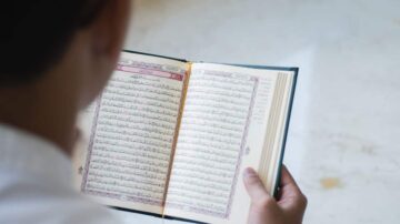 شاب يحمل مصحفًا مفتوحًا، يظهر النص العربي بوضوح. الخلفية بسيطة وغير مشوشة. يركز المشهد على الكتاب المقدس، مما يعكس أهمية القراءة الروحية.