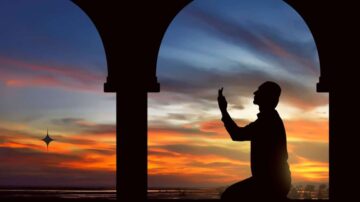 رجل يصلي في وضع الدعاء تحت أقواس مع غروب الشمس الملون في الخلفية، يعكس لحظة تأمل روحاني.