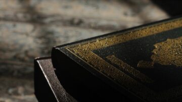 كتاب ذو غلاف أسود مزخرف بالذهب، موضوعة على سطح ذو نقوش بارزة. الإضاءة الخافتة تبرز تفاصيل الغلاف.