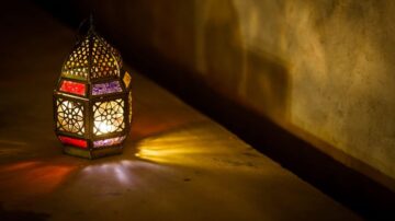 فانوس مزخرف بألوان زاهية، مضاء من الداخل، يظهر على سطح مائل مع ظلال جميلة تتشكل حوله.