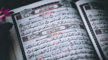 نصوص عربية من القرآن الكريم تظهر في كتاب مفتوح، مع تزيين فني وألوان دافئة، مما يعكس جمال الخطوط والتصميمات الإسلامية.