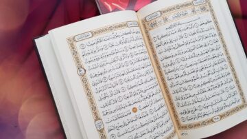 كتاب مفتوح يحتوي على نصوص باللغة العربية، مع تزيينات ملونة، يظهر جزءًا من القرآن الكريم. الخلفية مزخرفة بألوان دافئة، مما يبرز جمال الصفحة.
