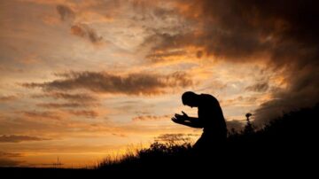 رجل يسجد في غروب الشمس مع سماء مليئة بالسحب الملونة، يعبر عن التأمل والسكينة في لحظة روحية.