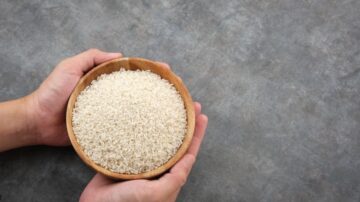 وعاء خشبي يحتوي على أرز أبيض، تُمسكه يدان. الخلفية رمادية.