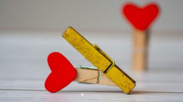 مشبك خشبي أصفر مع قلب أحمر صغير مثبت عليه، مع مشبك آخر في الخلفية يحمل نفس الشكل. تصميم بسيط ورومانسي يناسب ديكورات الاحتفال بالحب.