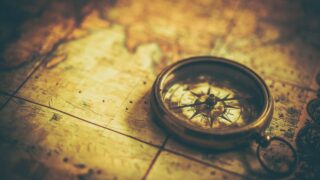 Vintage brass compass on aged world map, needle pointing north, casting soft shadows.