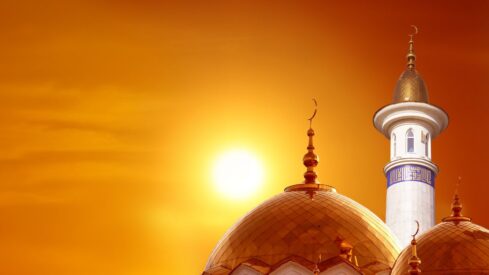 Mosque with golden domes and minaret under orange sunset sky, crescent moons visible.