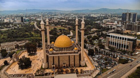 مسجد كبير بقبة ذهبية وأربع مآذن محاط بمناظر طبيعية ومبانٍ متعددة الطوابق.