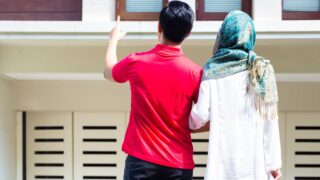 Rear view of two people, one in red pointing, the other in white with a patterned headscarf.