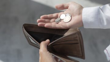 يد تحمل عملات معدنية بينما تُظهر محفظة فارغة، تعبير عن الندرة المالية أو الحاجة إلى إدارة الأموال.