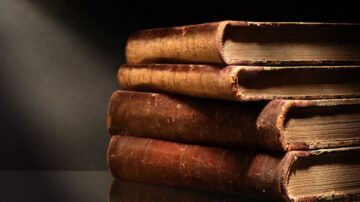 كتب قديمة ذات غلاف جلدي بني، موضوعة بشكل مرتب، مع تفاصيل دقيقة على الحواف. الإضاءة تبرز texture الجلد، مما يضيف طابعاً تاريخياً للكتب.