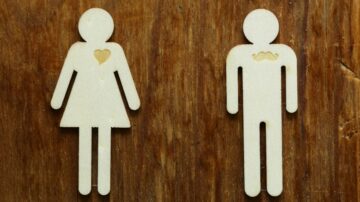 شخصيات خشبية تمثل رجل وامرأة، مع قلب محفور على صدر المرأة وشارب محفور على صدر الرجل، موضوعة على خلفية خشبية.