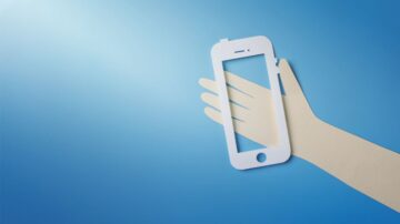 يد تظهر ورقة مقصوصة على شكل هاتف ذكي أبيض، مع خلفية زرقاء. التصميم يعكس مفهوم التكنولوجيا الحديثة والابتكار في الهواتف المحمولة.
