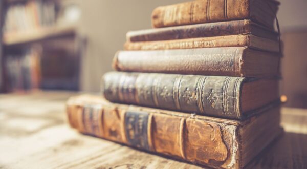 مجموعة من الكتب القديمة المكدسة بشكل مرتب على طاولة خشبية، تظهر تفاصيل الغلاف والتآكل، مما يعكس تاريخها وقيمتها الثقافية.