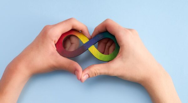 يد تحمل شكل رمز اللانهاية الملون بالأحمر والأصفر والأخضر والأزرق، مع تشكيل يد أخرى على شكل قلب، على خلفية زرقاء. تعبر الصورة عن الحب والتواصل والدعم.