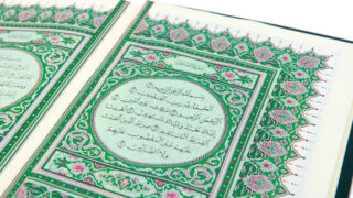 صفحة من القرآن الكريم مزينة بزخارف ملونة، تحتوي على نصوص عربية بخط واضح. التصميم يتضمن تفاصيل نباتية وأشكال هندسية، مما يعكس الفن الإسلامي التقليدي.