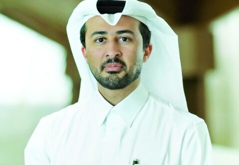 رجل يرتدي الثوب القطري والغترة، يقف في مكان داخلي مضاء. يظهر تعبيره الجاد وثقته في النفس، مع خلفية غير واضحة تركز على الشخصية.