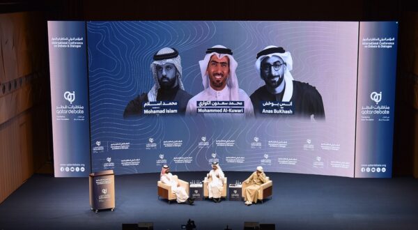 مؤتمر معلوماتي في الدوحة يضم جلسة حوارية مع محمد إسلام ومحمد الكواري وأنس البتّاش، حيث يتحدث المتحدثون عن مواضيع تكنولوجية حديثة. يظهر في الخلفية شعار المؤتمر.