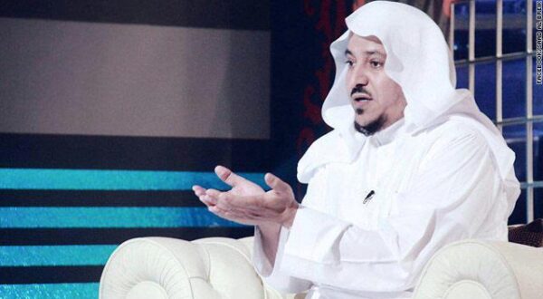 رجل يرتدي عباية بيضاء وعقال، يجلس على أريكة بيضاء ويتحدث بيديه في برنامج حواري، مع خلفية ملونة.