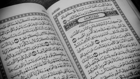 Open pages of an Arabic book with intricate calligraphy and decorative borders, featuring religious text. The book appears to be a Quran, emphasizing its cultural and spiritual significance.