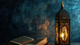 Decorative lantern casting warm light beside an open book with intricate designs, set against a textured blue background.