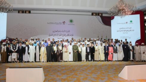 مجموعة من الشخصيات البارزة في مؤتمر دولي، يقفون معًا على خشبة المسرح، يرتدون ملابس رسمية. الخلفية تحتوي على شعارات ومعلومات حول الحدث، مع تصميم أنيق. يُظهر الصورة التنوع والالتزام بالعمل المشترك في مجال التعاون الدولي.