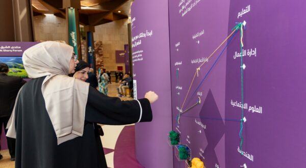امرأتان تتفاعلان مع لوحة معلومات في منتدى شراكة، حيث تشير إحداهما إلى مسارات تعليمية ومهنية متعددة، مع وجود مواد ملونة في الأسفل.